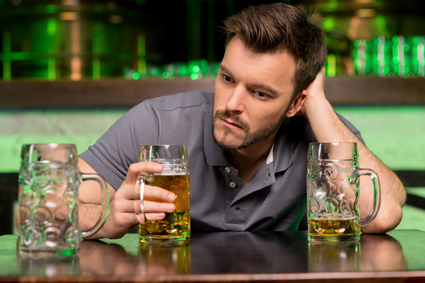 Lonely man in bar. Depressed young man drinking beer and holding hand in hair while sitting in bar